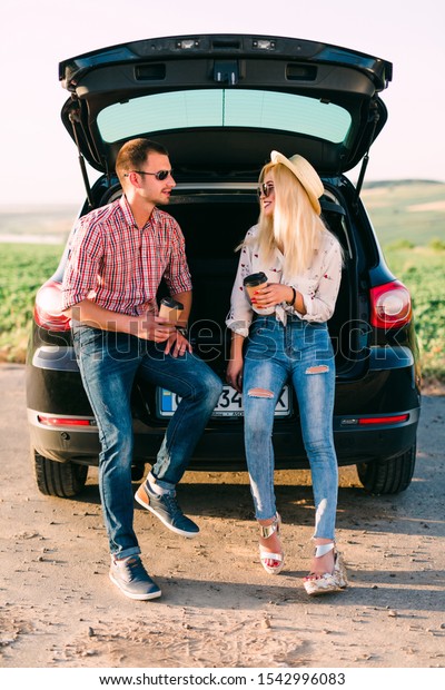 Beautiful couple\
sitting with coffee in car\
trunk