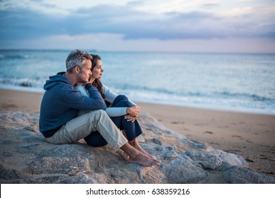 Beautiful couple sitting on a rock at the beach watching the sunset. They wear casual clothes - Powered by Shutterstock