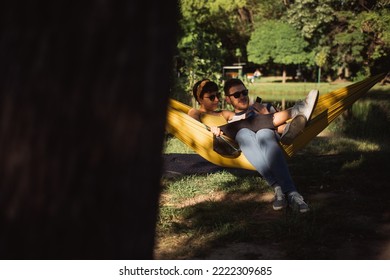 Beautiful Couple Sitting On The Yellow Hammock While Holding A Polaroid Camera And Looking At The Picture