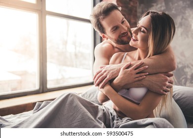 Beautiful Couple Is Smiling And Hugging While Spending Time Together In Bed At Home. Man Is Kissing His Girlfriend