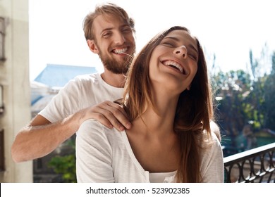 Beautiful couple standing at balcony. Man making massage his girlfriend.