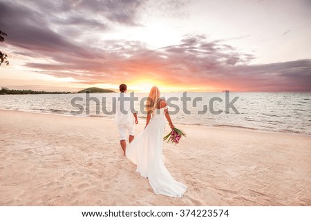 beautiful couple at sunset near the ocean.Honeymoon romantic couple in love holding hands walking on beautiful sunset at beach. Lovers or newlywed married young couple by the sea. Wedding in Thailand.