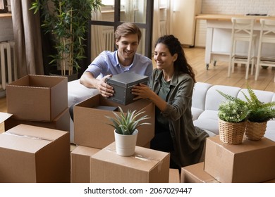 Beautiful couple taking out belongings from boxes at relocation day  enjoy unpacking process sit sofa in living room  Bank loan   mortgage  housing improvement  happy homeowners family concept