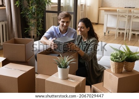 Beautiful couple taking out belongings from boxes at relocation day, enjoy unpacking process sit on sofa in living room. Bank loan and mortgage, housing improvement, happy homeowners family concept