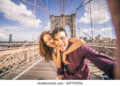 Beautiful couple taking selfie on Brooklyn Bridge, New York - Tourists having fun and photographing NY landmarks - Powered by Shutterstock