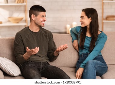 Beautiful couple talking, sitting on couch at home, have a nice conversation at their cozy apartment