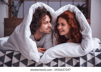 Beautiful couple is talking and smiling while lying in bed wrapped in blanket - Powered by Shutterstock