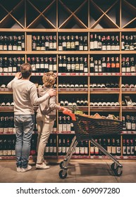 Beautiful couple is talking and smiling while choosing wine at the supermarket