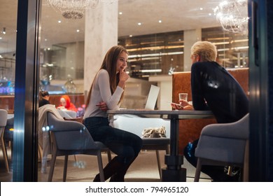 Beautiful Couple Of Two Young Adults Meet For Coffee At Downtown Restaurant Or Bar. Discuss Relationship Issues And Problems. Nightlife Snapshot From Outside Cafe Window