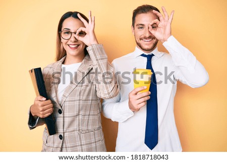 Beautiful couple wearing business clothes drinking take away coffee holding folder smiling happy doing ok sign with hand on eye looking through fingers 