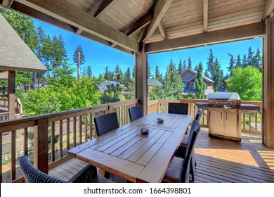 Beautiful Covered Deck With Large Luxury Dining Room Table With Grill And Railings. Lots Of Pine Trees.