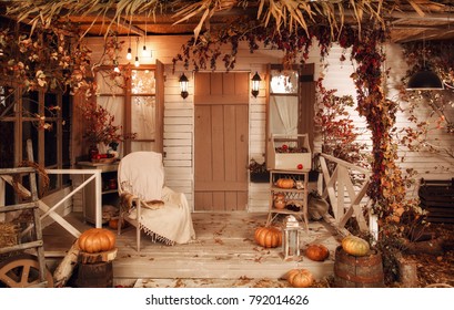 Beautiful Cozy Wooden Porch Of The House With A Chair And Pumpkins In Autumn Time. Halloween Design Courtyard, Lit By Flashlights, With Dry Fall Leaves.