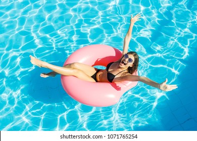 Beautiful crazy woman relaxing on inflatable ring in blue swimming pool.