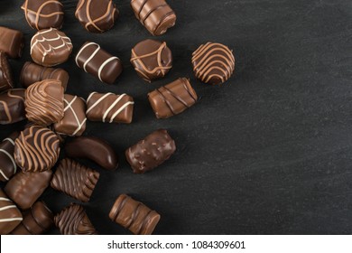 Beautiful Creative Chocolate Sweets on Natural Black Stone Background. Scattered Chocolates Top View and Flat Lay with Place for Text