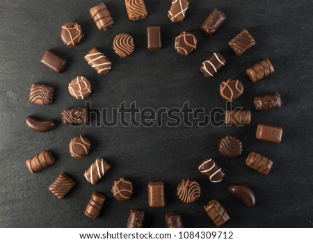 Beautiful Creative Chocolate Sweets on Natural Black Stone Background. Mix of Chocolates in Round Frame Shape Top View and Flat Lay with Place for Text
