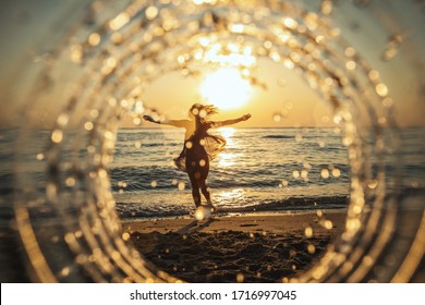 A beautiful creative composition of a sea landscape shot through a circle focus showing a young woman who is having fun on the beach in sunset.