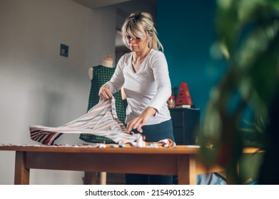 Beautiful Creative Woman Tailor Cutting Textile On The Table At Home. Seamstress Working At Home. Dress Maker Working At Home And Creating Beautiful High Fashion Dress. Fashion Designer.