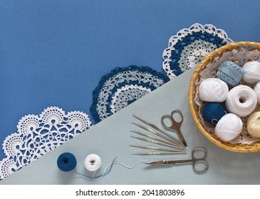 Beautiful crochet lace doilies. Balls of cotton yarn for hand crochet in wicker basket and set of hooks of different sizes on blue and gray background. Flat lay, copy space, close-up, top view, mockup