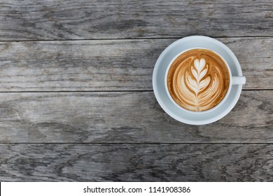 A beautiful cup of cappuccino with latte art in the wooden space background. Trendy toning. Minimal composition, hipster vibes. Top view, flat lay copy space for your text.