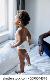 Beautiful Curious Black Dark Skinned Child Girl Stand On Bed Looking Through The Window, Interested In Something, In Contemplation. Kid In Diapers. Children Emotions, Lifestyle Concept