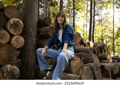 Beautiful curly brunette smiling and sitting on logs in the forest - Powered by Shutterstock