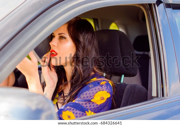 Beautiful curly brunette woman sit in\
auto on a road and correct make up, dangerous for\
woman
