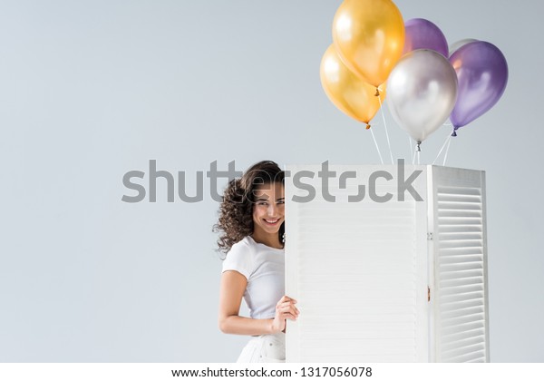 Beautiful curly girl with air balloons smiling\
on grey background