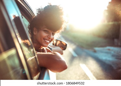 Beautiful curly hair woman enjoying the breeze, looking out of the window's car while having a road trip - Powered by Shutterstock