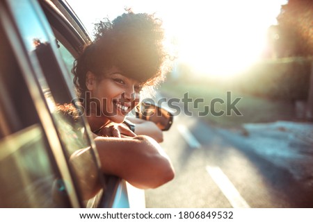 Beautiful curly hair woman enjoying the breeze, looking out of the window's car while having a road trip