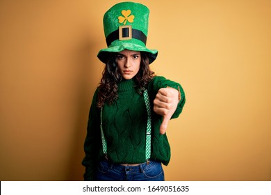 Beautiful Curly Hair Woman Wearing Green Hat With Clover Celebrating Saint Patricks Day Looking Unhappy And Angry Showing Rejection And Negative With Thumbs Down Gesture. Bad Expression.