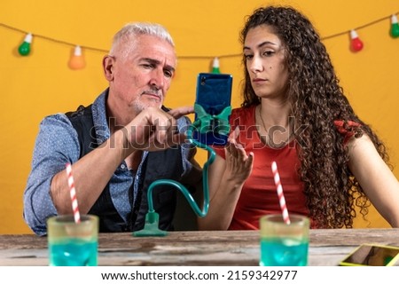 beautiful curly haired woman and his father chatting with the smartphone hanging on a phone holder - studio shot