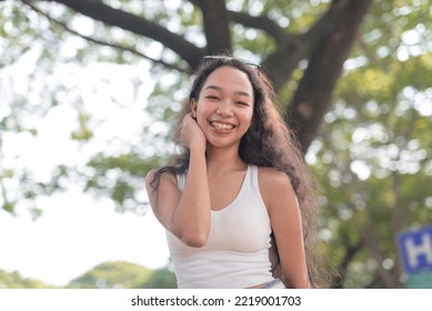 A Beautiful Curly-haired Filipina Smiles For The Camera On A Hot Afternoon Outside The Garden.