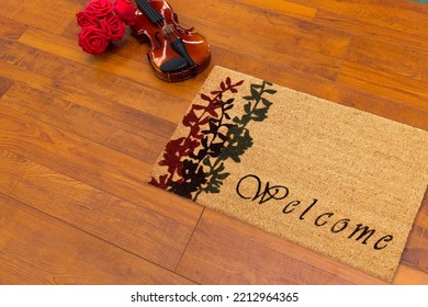 Beautiful Cursive Welcome Peach Color Doormat With Red And Black Flower Plant Placed With Guitar And Red Roses