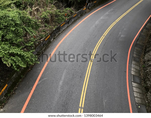 Beautiful curve road with red and yellow\
divided lanes, water drain, in\
countryside