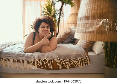 Beautiful Curvy Oversize African Black Woman Afro Hair Lying On Bed Eco Friendly Cozy Bedroom Interior Design With Home Plants. Body Imperfection, Body Acceptance, Body Positive And Diversity Concept.