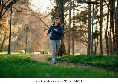 A Beautiful Curvy Woman Runs In A Nature Park At Sunset.