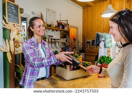 Beautiful customer girl paying for shopping at checkout in a grocery store - Young woman taking a credit card from a customer in a biologic market
