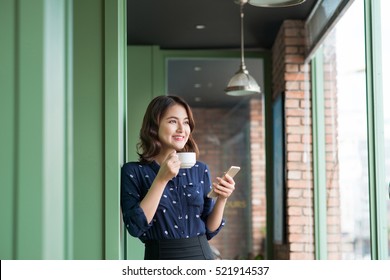 Beautiful cute asian young businesswoman in the cafe, using mobile phone and drinking coffee smiling