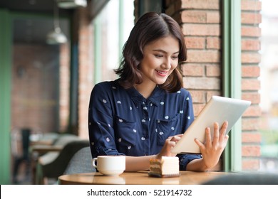 Beautiful cute asian young businesswoman in the cafe, using digital tablet and drinking coffee smiling