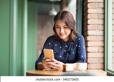 Beautiful cute asian young businesswoman in the cafe, using mobile phone and drinking coffee smiling - Powered by Shutterstock