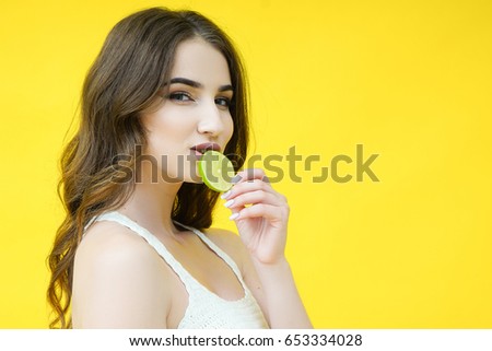 Beautiful cute brunette girl with a lime slice near the face isolated on a yellow background
