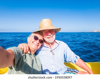 Beautiful And Cute Couple Of Seniors Or Old People In The Middle Of The Sea Driving And Discovering New Places With Small Boat. Mature Woman Holding A Phone And Taking A Selfie With Hew Husband