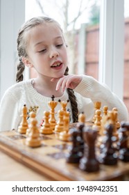 Beautiful cute genius child young girl playing chess strategy with wooden pieces on chessboard kid concentrating planning move with king and queen for checkmate