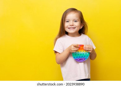 A beautiful cute girl holds a colored pop toy in her hands and smiles. Yellow background. Anti-stress, emotions, good mood. A place for text. Trend. High quality photo - Shutterstock ID 2023938890