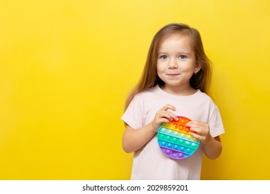 A beautiful cute girl holds a colored pop toy in her hands and smiles. Yellow background. Anti-stress, emotions, good mood. A place for text. Trend. High quality photo - Shutterstock ID 2029859201