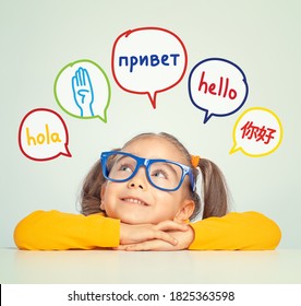 Beautiful Cute Little Girl With Eyeglasses Looking At Hello Word In Spanish, English, Russian, Chinese And American Sign Language In Speech Balloons. K-12 Foreign Language Learning Concept.