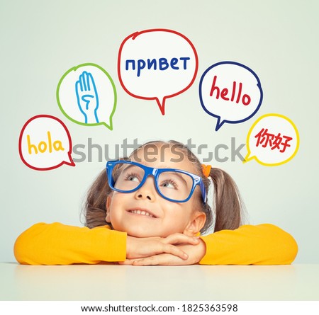 Beautiful cute little girl with eyeglasses looking at hello word in spanish, english, russian, chinese and american sign language in speech balloons. K-12 foreign language learning concept.