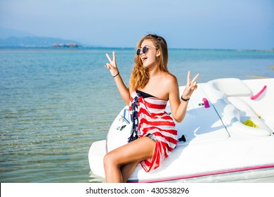 Beautiful cute sexy cheeky hipster blonde girl near a speed boat, wrapped in a scarf with a print of the American flag, lifestyle trendy sunglasses healthy tanned skin, hair, full lips, crazy emotions