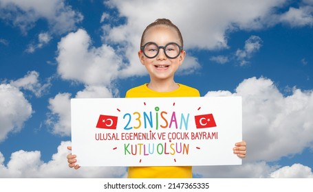 Beautiful cute Turkish girl holding a  paper with national holiday celebration message in front of cloudy sky. 23 Nisan Kutlu Olsun. English: Happy April 23 National Sovereignty and children's day.