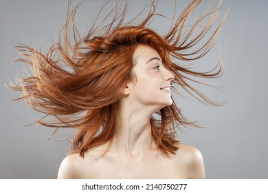 Beautiful dark burnt orange windy hair girl smiling. Studio portrait with happy face expression against gray background.